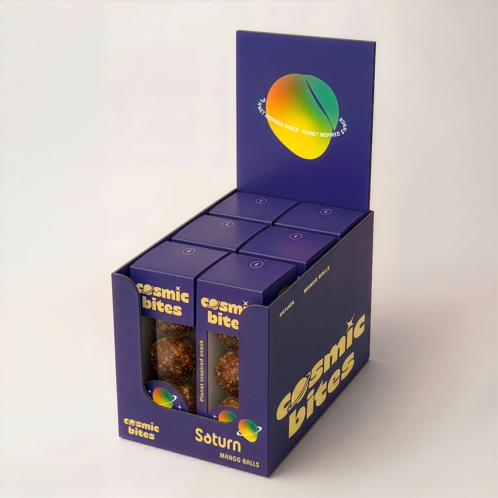 Ein Tray Cosmic Bites Energy Balls der Sorte Mango ist zu sehen, das sechs einzelne Packungen enthält. Die gelben Bälle sind dem Planeten Saturn nachempfunden, wonach die Sorte benannt ist. Der gesunde Snack besteht aus rein natürlichen Zutaten, ist vegan, hat keinen zugesetzten Zucker und einen stark reduzierten Dattelanteil von nur 25%.