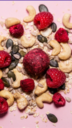 Knallig roter Cosmic Bites Energy Ball inspiriert vom Planeten Mars, umgeben von frischen Himbeeren, Cashews und Kernen – leckerer gesunder Snack mit wenig Datteln.
