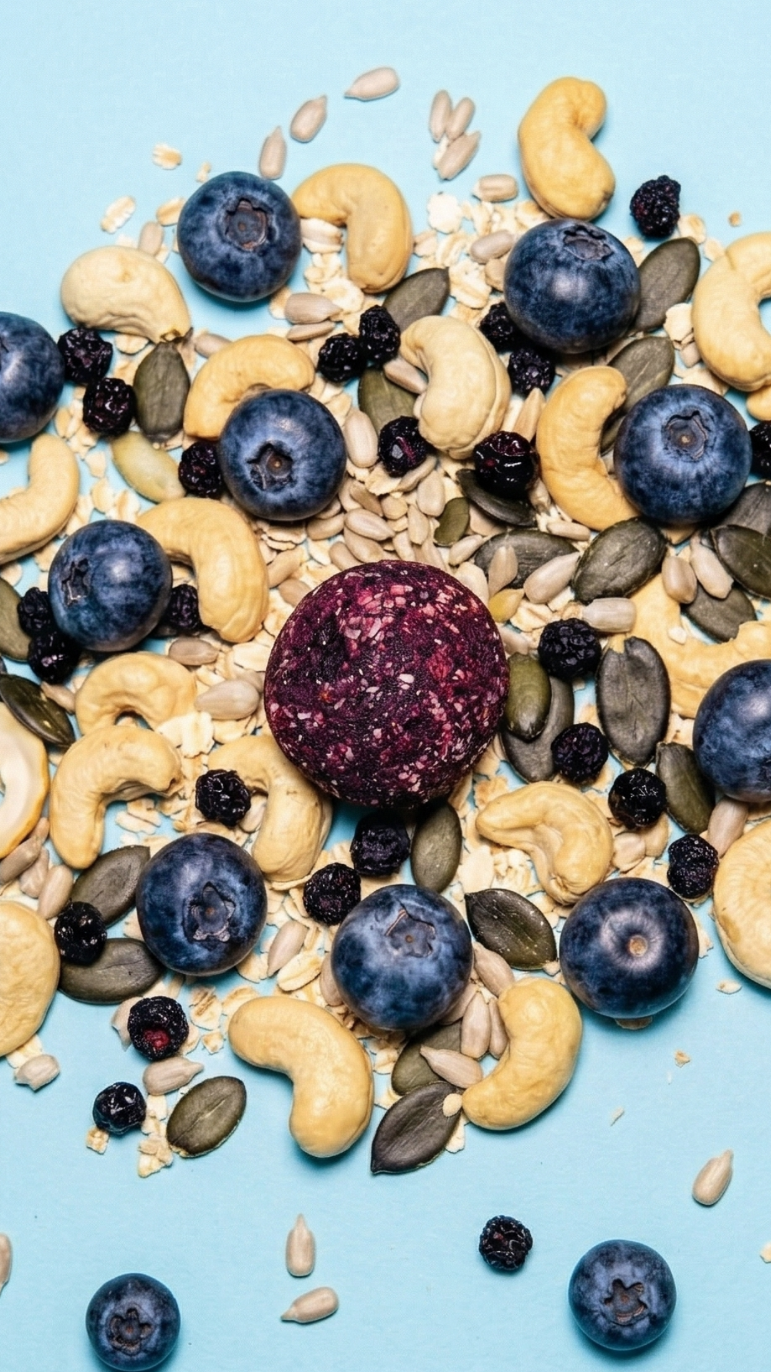 Tiefvioletter Cosmic Bites Energy Ball inspiriert vom Planeten Neptun von Heidelbeeren, Cashews und Kürbiskernen umgeben – gesunder Snack ohne Zuckerzusatz und mit wenig Datteln.
